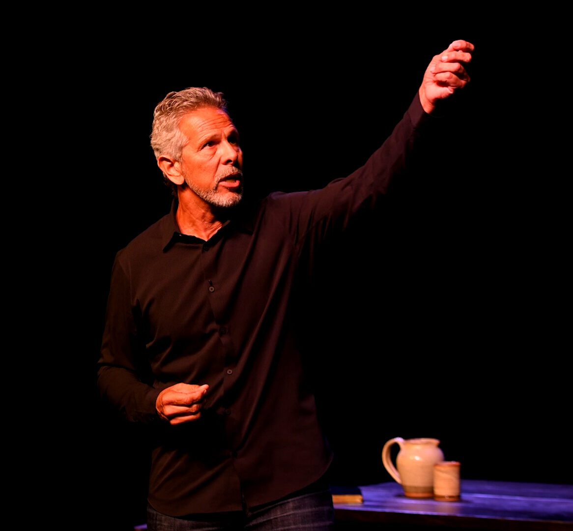 A man standing on stage holding his hand up.