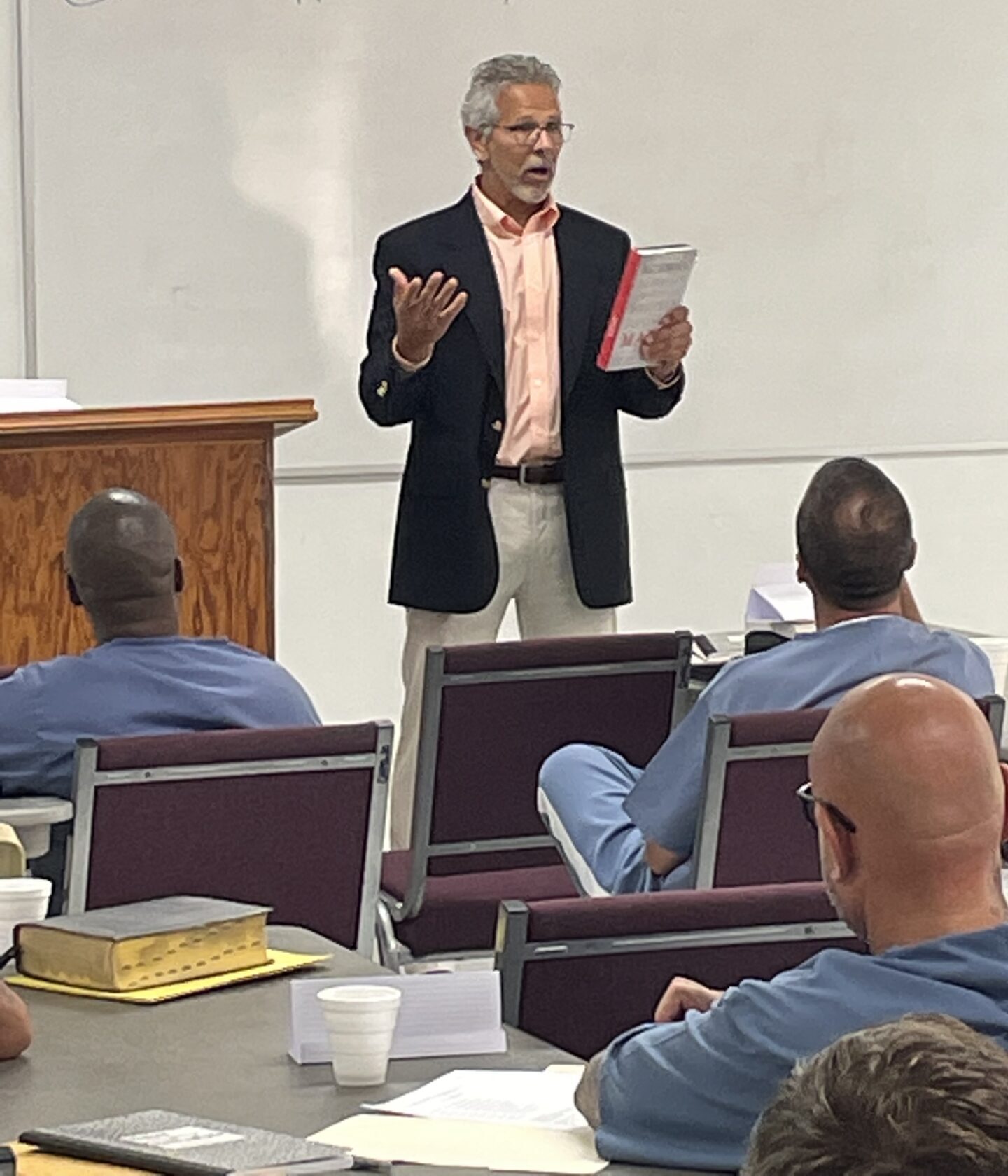 A man in a suit is giving a lecture to people.