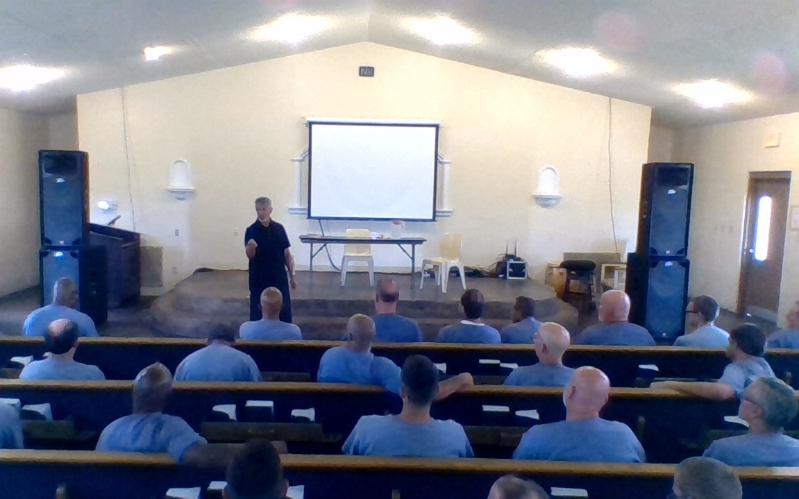 A man in blue shirts is giving a lecture to people.